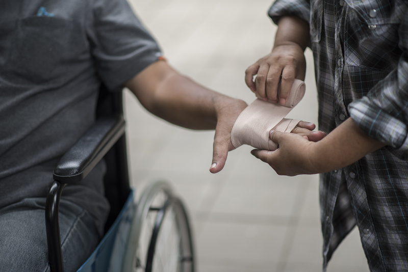 Women are wrapping hands on men sitting on wheelchair patients with bandages.